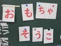 写真：おもちゃそうこ　と文字を描いた紙が貼られている黒板