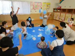 写真:青いビニールシートの周りを親が囲んで、中で子供が遊んでいる様子