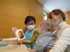 写真：お母さんに抱かれた赤ちゃんに絵本を読み聞かせする様子