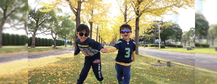 銀杏並木の前でサングラスをかけた2人の子供が手を繋いでいる