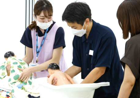 お父さんが人形の赤ちゃんを使って沐浴の練習をしている写真